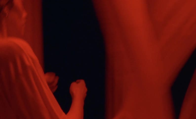 A woman is running through sheets hanging on clotheslines at night with a red light on