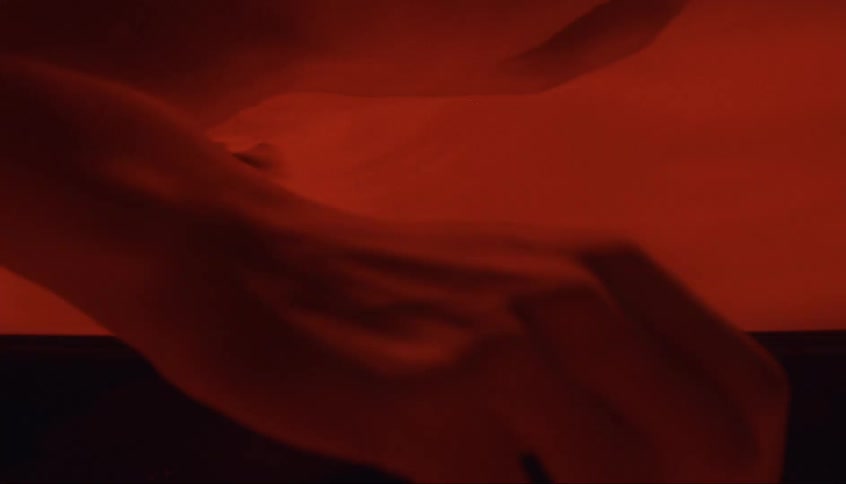 A red liquid substance is rippling and a hand emerges and reflects on the surface