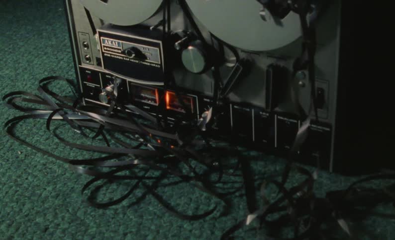 Person kneels on floor next to tape player that is mangling and eating the tape on the spool