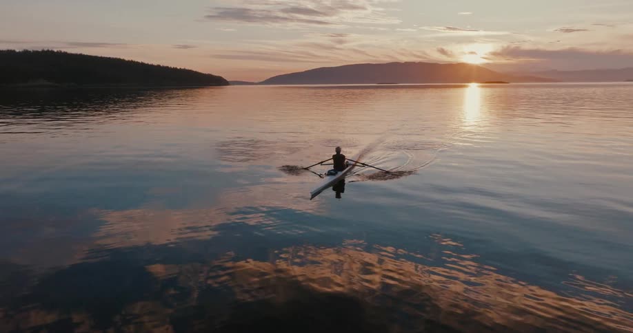 Person rows on kayak as sun cresting over mountains on distant shore reflect off the shimmering water