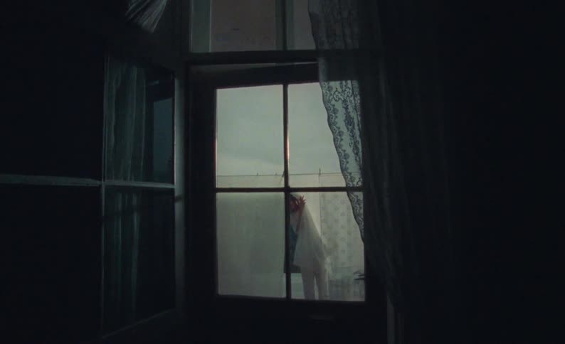 Window shows woman hanging sheets on clothesline