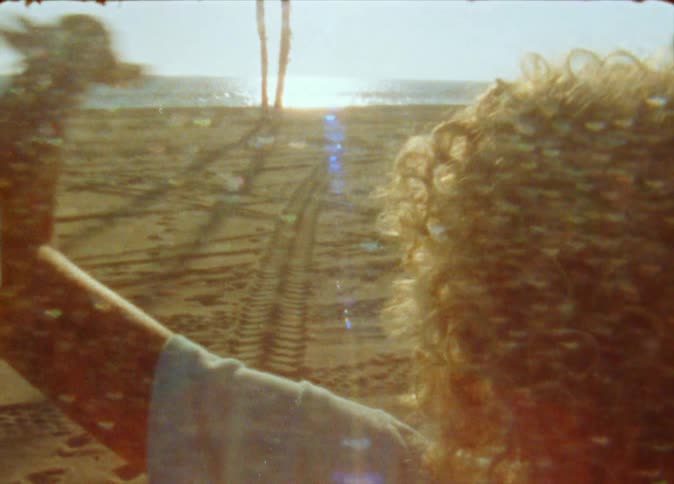 A girl balances on a skateboard as she stands on the beach and raises her arms above her head
