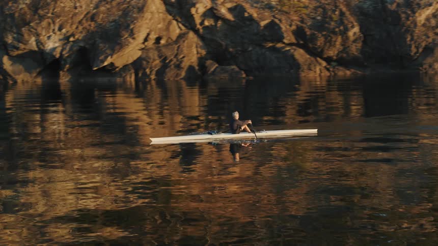 A man paddles his boat backward in a lake below a canyon