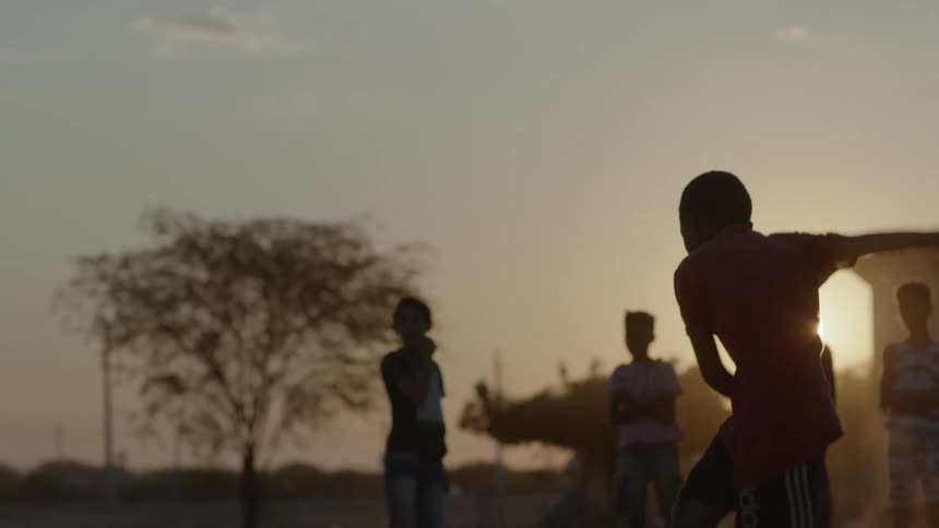 The silhouette of a boy running to kick a soccer ball while his friends stand watching