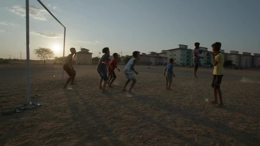 A group of young boys playing soccer barefoot on a dirt field