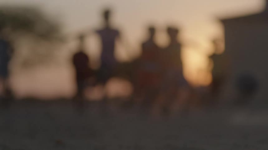 A ball sits on the ground and someone kicks it and a group of boys start playing