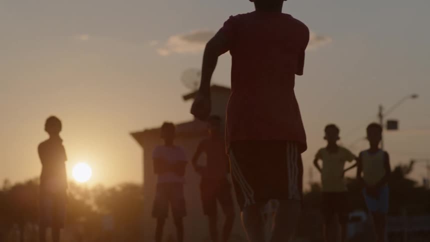 Youth kicks soccer ball as he and others are silhouetted by the sun