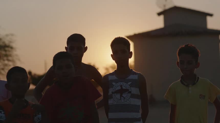 A group of boys standing in a line posed with the sun setting and glaring behind them