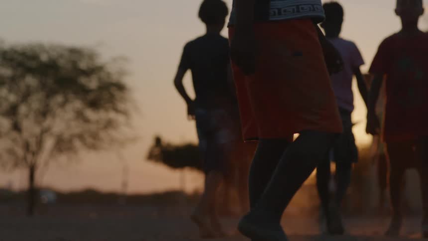 A group of barefoot boys walk together outdoors at sunset