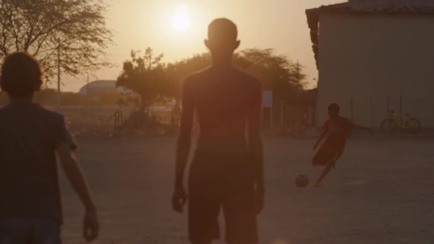 A group of boys are playing ball in the yard and another boy rides his bicycle where they are playing