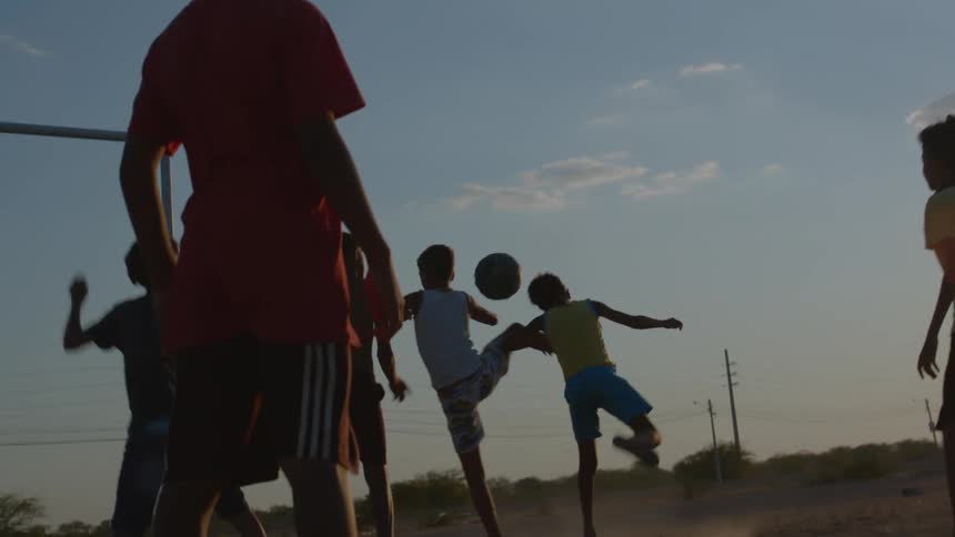 A group of boys is playing soccer on a dirt field