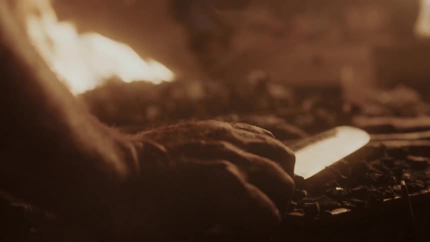 A person picks up a knife near a fire