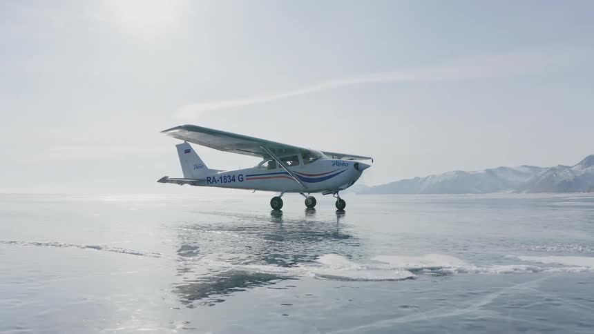 A pilot starts up a small plane parked on ice covered ground