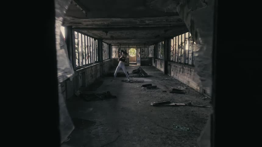A woman is shadow boxing inside a run down building