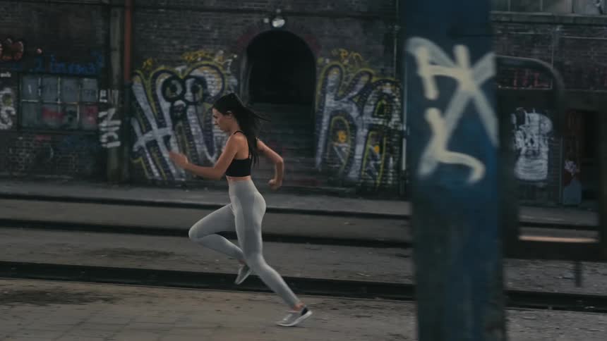 A woman is running past buildings covered in graffiti