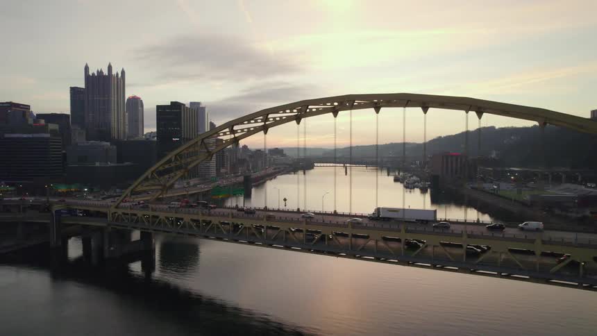 Traffic travels across a bridge spanning a river in a metropolis during the day