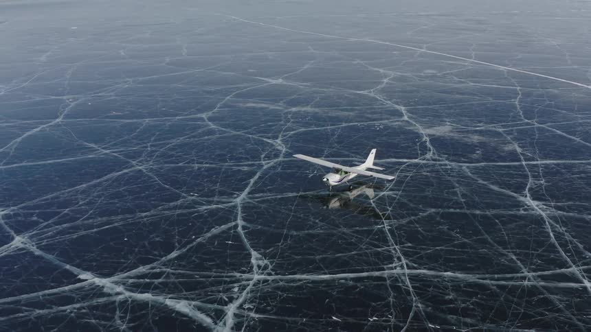 A plane is parked on a lake covered in solid ice in the mountains