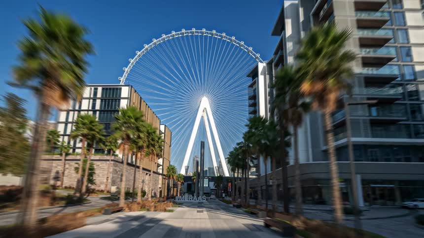 Traffic passes through a road that runs alongside apartment buildings and leads to a ferris wheel