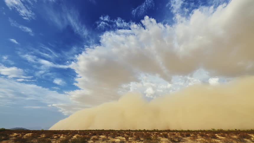 Dust storm flows across desert scrub with hills on the horizon