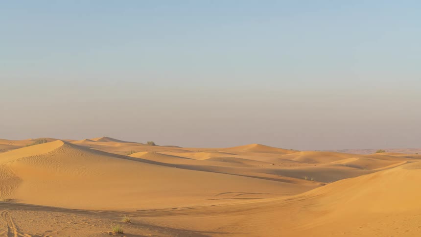 Sunlight shines on sand dunes in the desert as a shadow moves across the sand