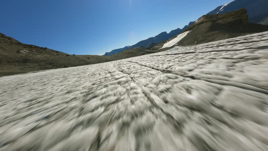 Intense aerial fly over the cracked surface of a glacier on the mountains under a clear blue sky