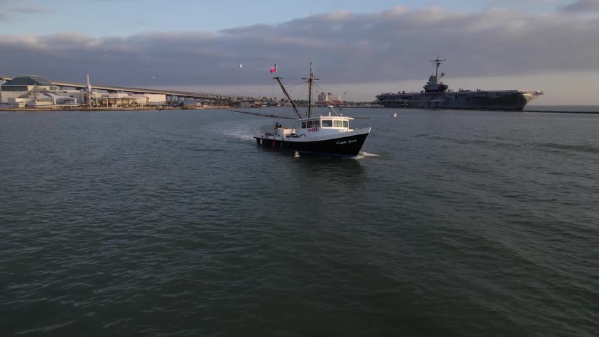 A shrimp fishing boat travels along a waterway off the coast of city during sunrise