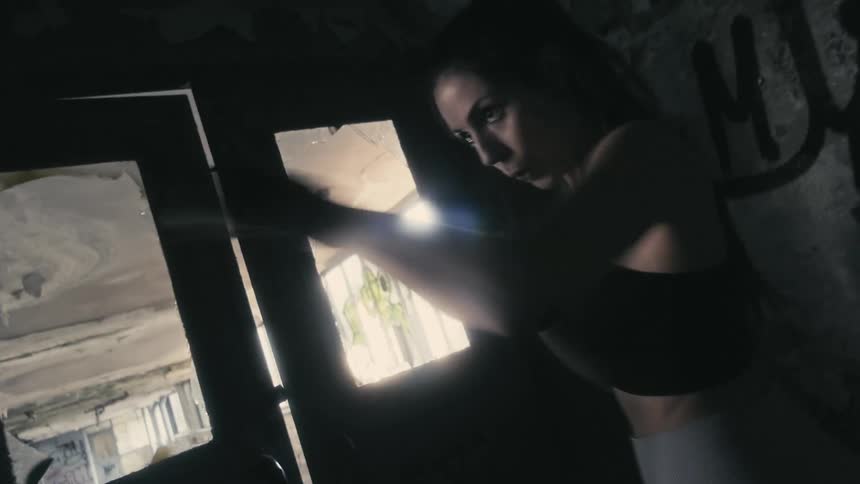 Woman with ponytail black sports bra and gray yoga pants do boxing training in building