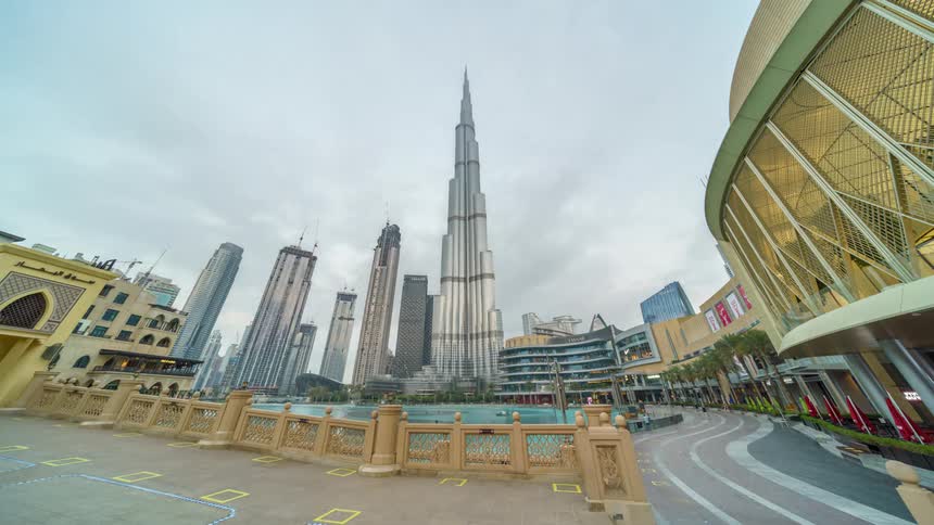 People are walking in a metropolitan city with modern towers and skyscrapers as the clouds move overhead and night becomes day