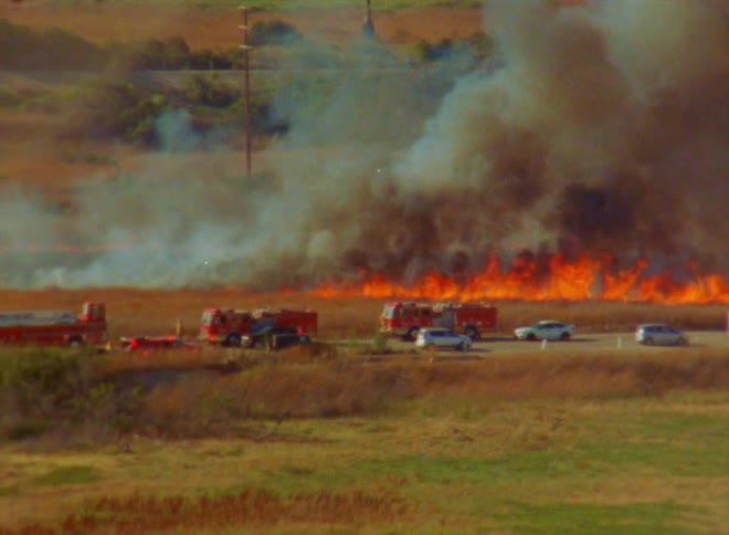 A field is on fire near a road with a lot of traffic and firetrucks