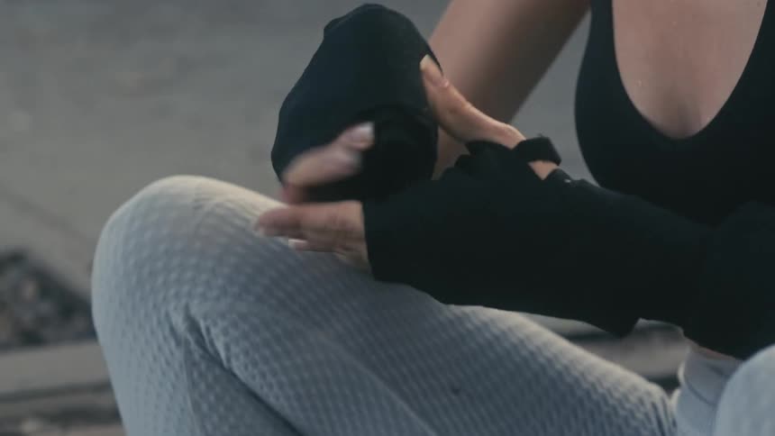 Woman sits on concrete steps wrapping her hands before working out