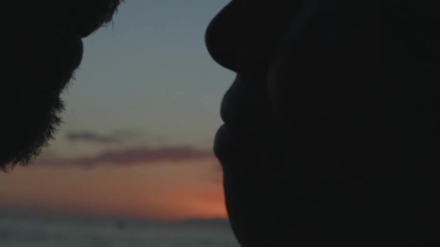 A man and woman kiss with the sunset behind them