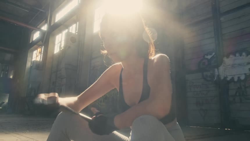 A woman is sitting on the floor of a room wrapping her wrist as the sun shines brightly in the window