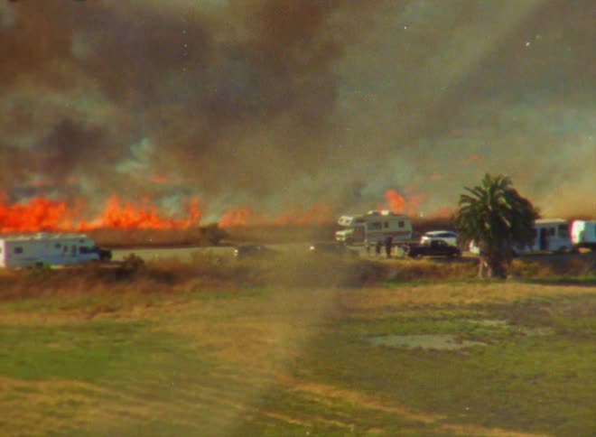 There is a fire outside and cars are driving by in the day time