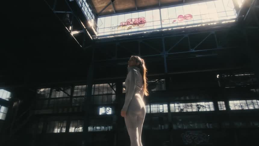 Woman stands in the middle of empty abandoned factory looking around graffiti covered building