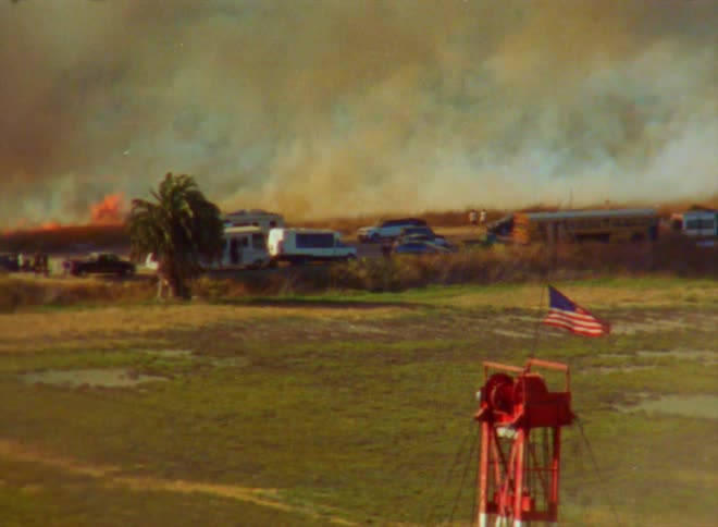 A fire is raging close to where several campers and vehicles are trying to leave