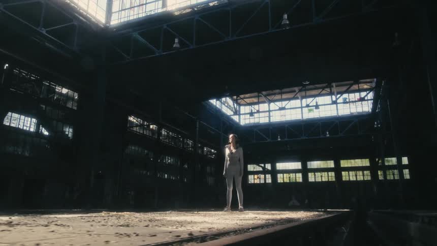 A woman stands in an empty building and looks straight ahead