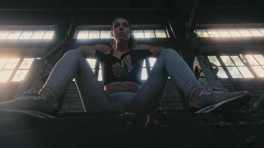 Young fit woman wearing sports clothes takes a break sitting on a staircase inside a warehouse