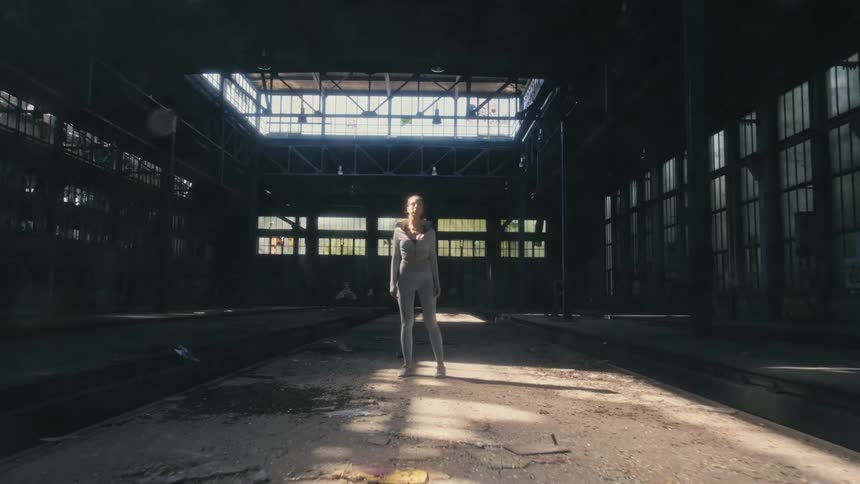 A woman stands in the middle of an empty warehouse