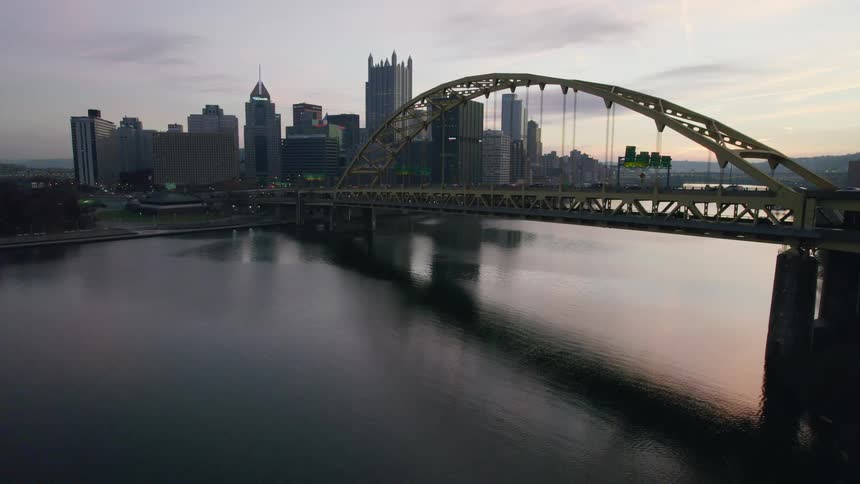 Traffic moves across a bridge leading into a big city with tall buildings and skyscrapers on the metropolitan skyline