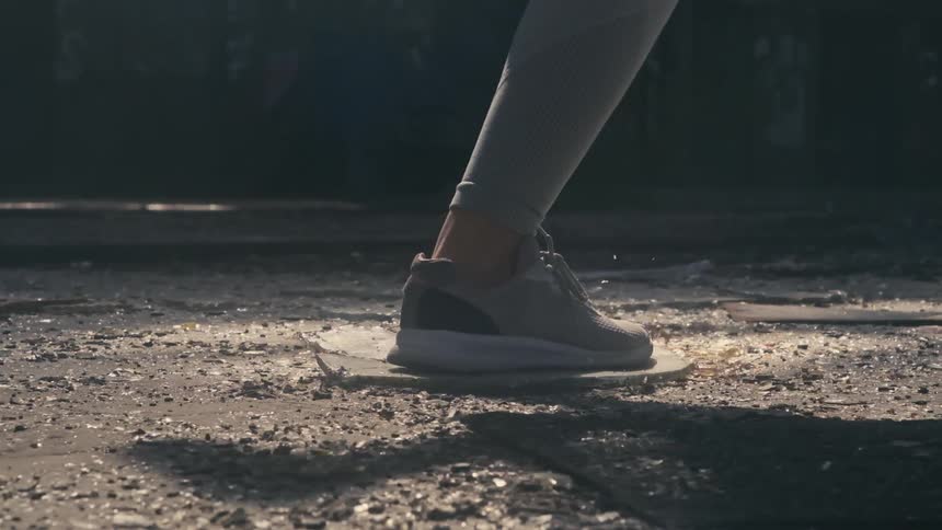 Close up of the foot of a woman jogging crushing a piece of plastic on the ground of an abandoned building