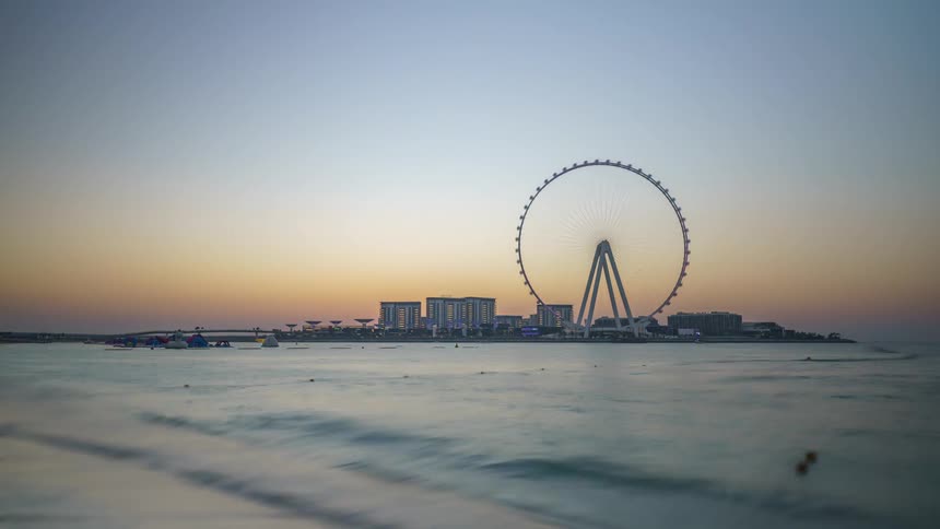 A large ferris wheel looms over the coast of a metropolis as the sun sets