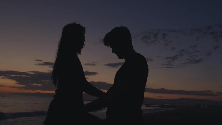 A man and woman on the beach hug and kiss one another