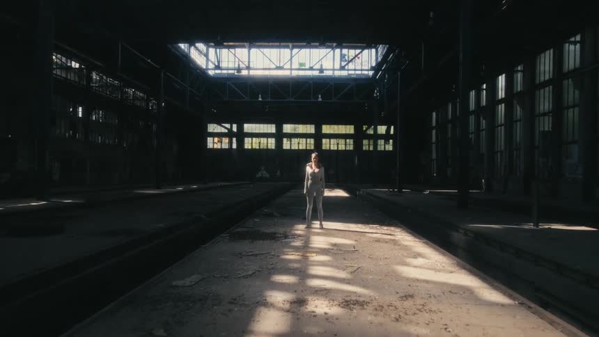 A woman stands next to train tracks in an abandoned train terminal