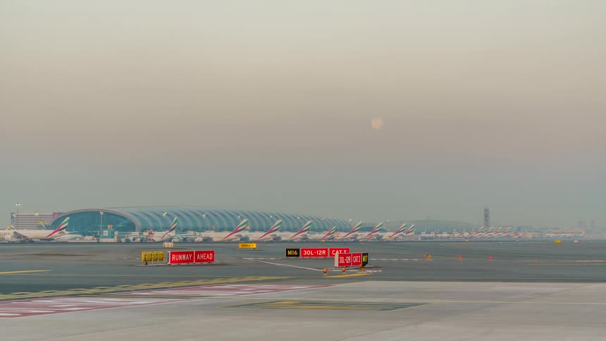 Exterior view of airport with planes taking off and landing with moon going down in the sky