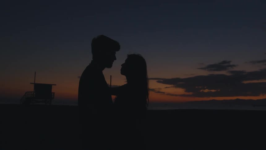 Man and woman making out on the beach is silhouetted against the red sky