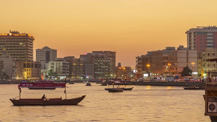Boats traveling on the dubai creek river with city buildings and traffic on shore