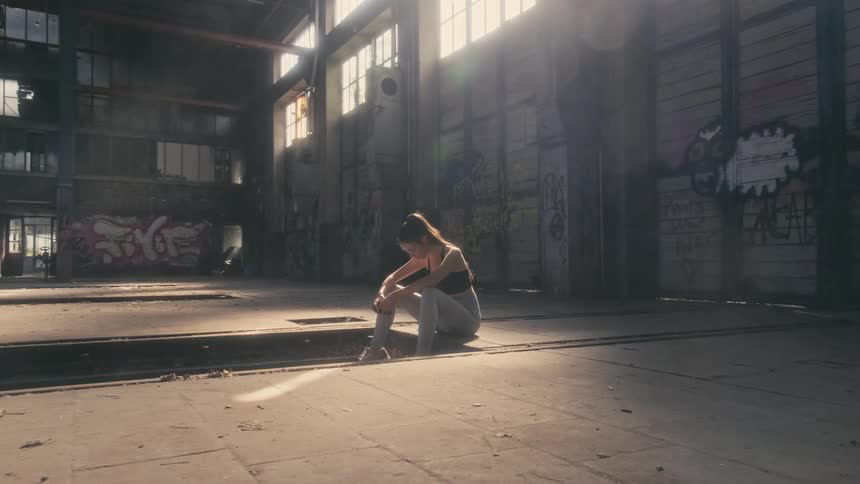 Woman sits on top of steps in abandoned warehouse covered with graffiti