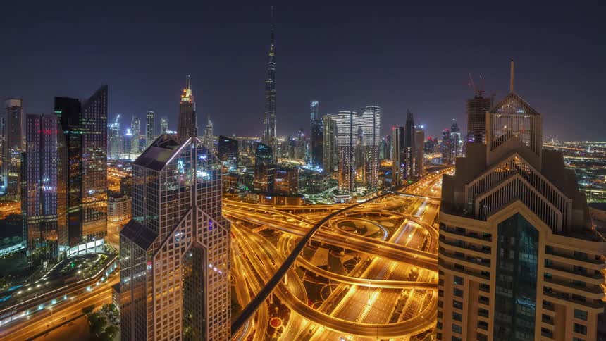 Time lapse of traffic and bright lights over a complex overpass on the streets of a futuristic skyline at night