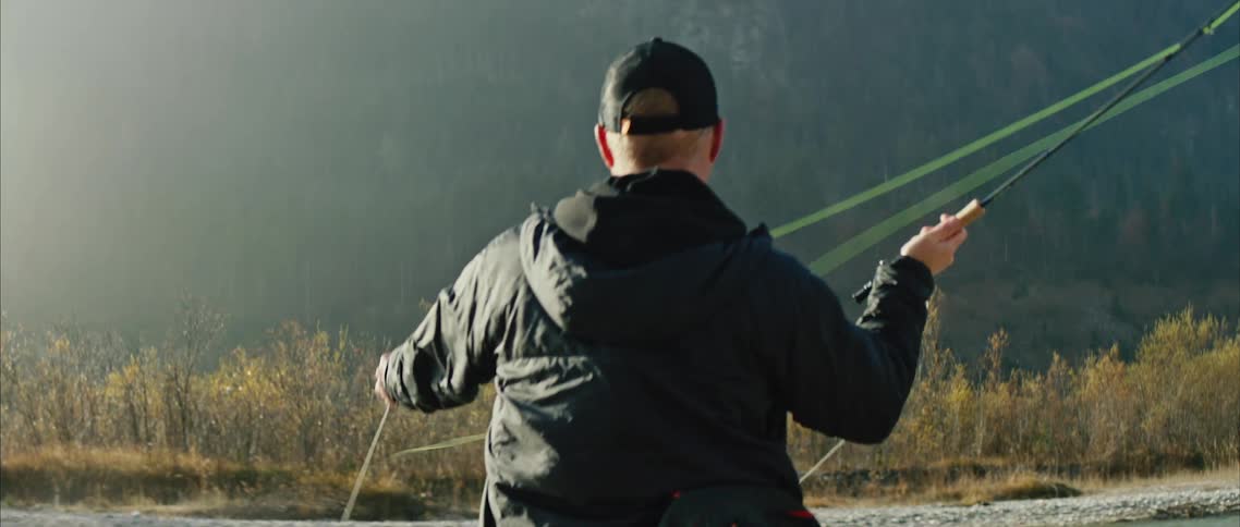 A fisherman casts their fishing line while fishing in a river during the day