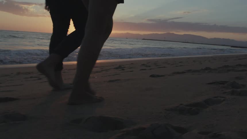 Two people are walking in the sand at the beach around the day time